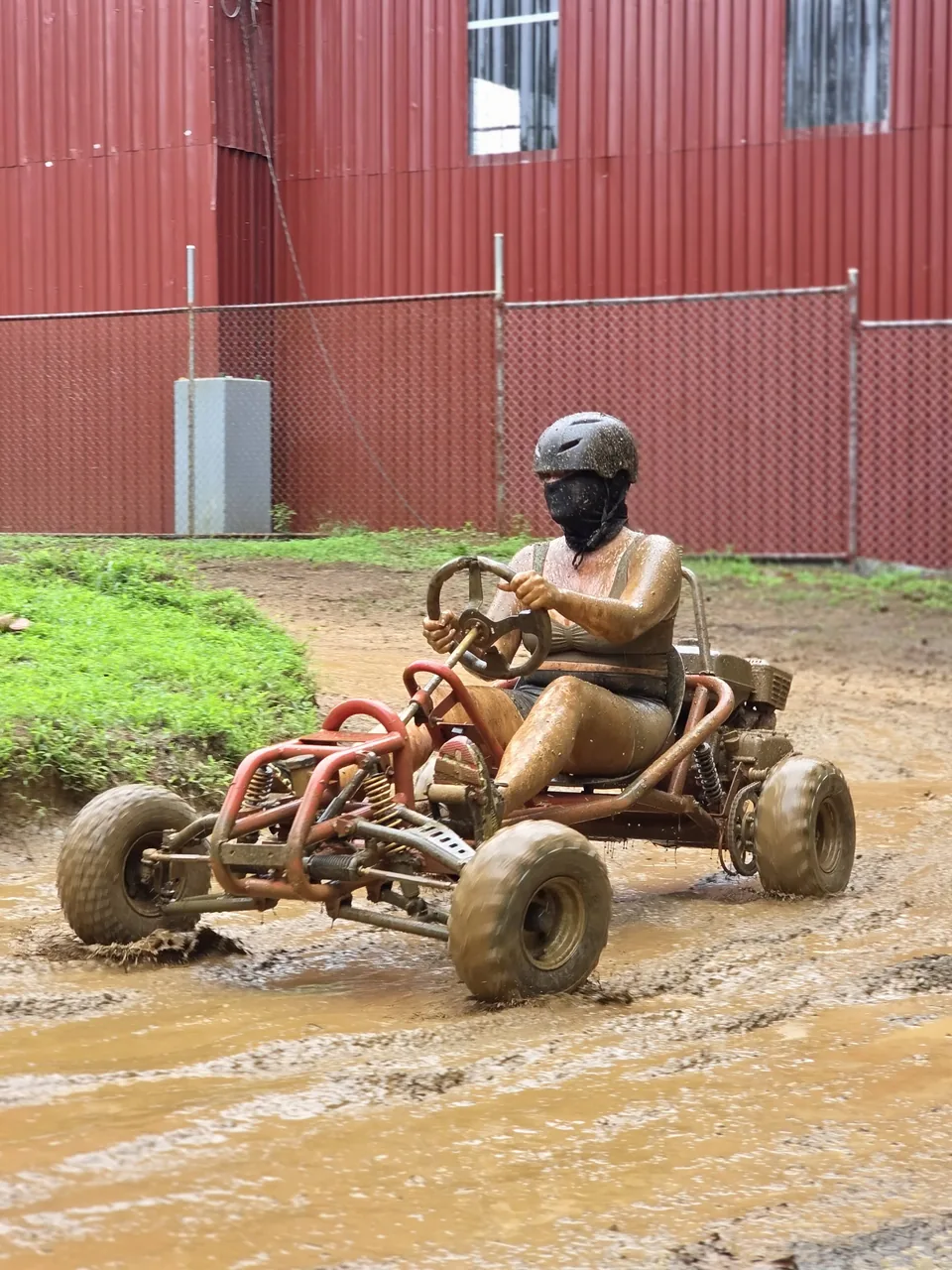 Piloto conduce su go kart junto a la bodega de lámina roja de las instalaciones de Sarapiquí Race Park